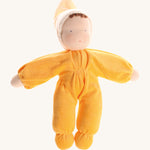 Grimm's Yellow Soft Doll is a hand-crafted Waldorf doll, wearing a yellow all-in-one baby grow with a matching night cap, with a smiling face and brown curls peeking out from under the yellow cap. The image is on a cream background