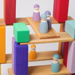 A closer view of the Grimm's 12 Pastel Friends wooden peg dolls, standing on natural wooden Grimm's building boards and colourful blocks
