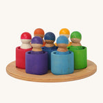 Grimm's 7 Rainbow Friends in Bowls, are an open ended, small world play toy with Grimms Friend peg dolls sat inside small wooden bowls. The Grimms Friends are removable from the bowls and can be used in open ended play. The colours of the Grimms Friends and bowls are red, purple, blue, orange, yellow, green and light blue, and are sat on a small wooden tray on a cream background.