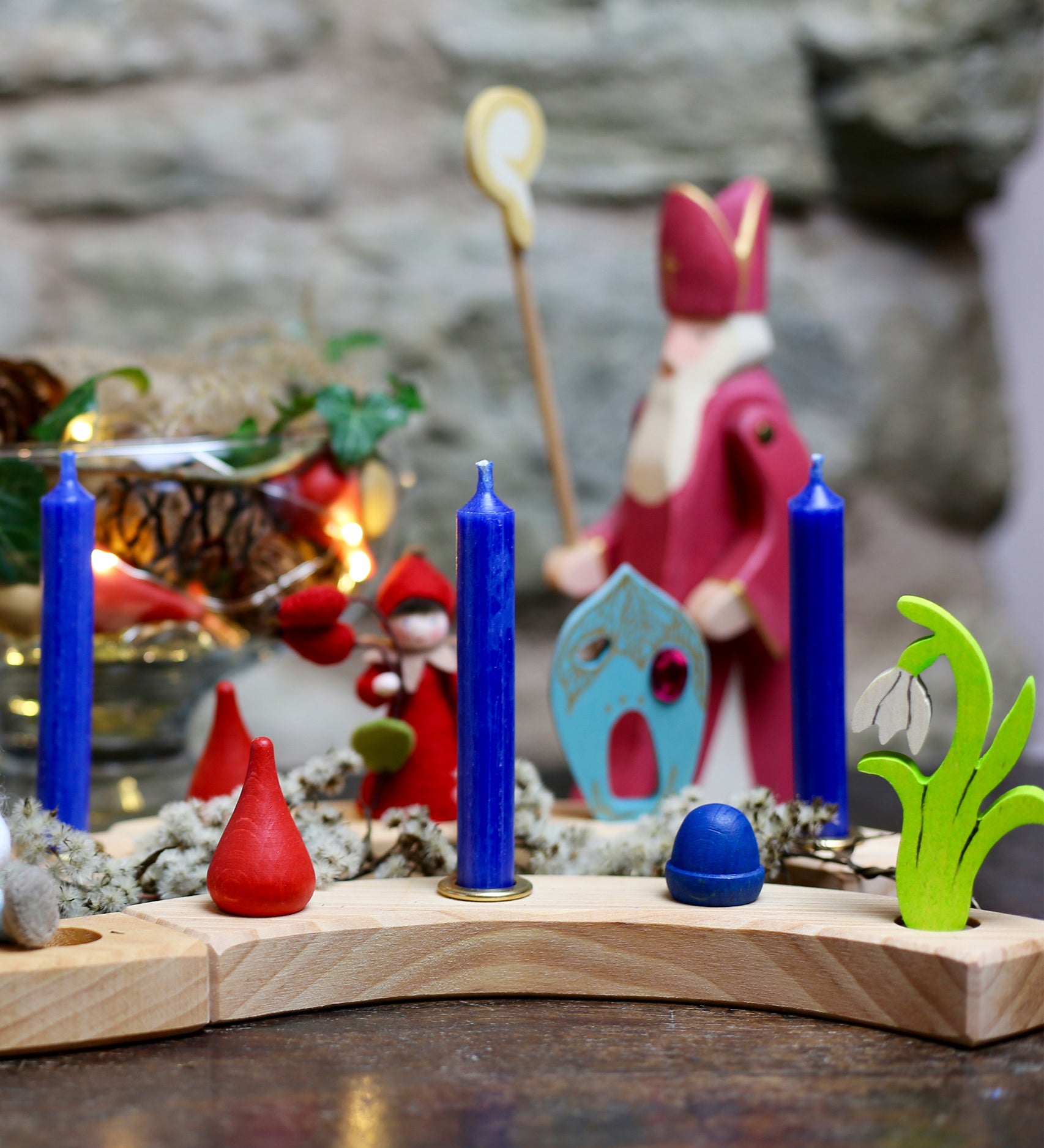 A lovely winter celebration display, made with a Grimm's Wooden Celebration ring. There are blue candles in brass holders, and colourful loose parts 