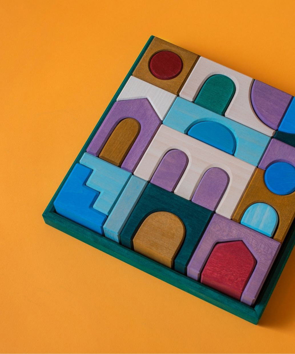 Grimm's wooden floor building set, shows handcrafted piece in a green frame on a orange background.