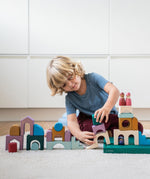 Child building using pieces from the Grimm's wooden floor set on the green frame on a fluffy carpet