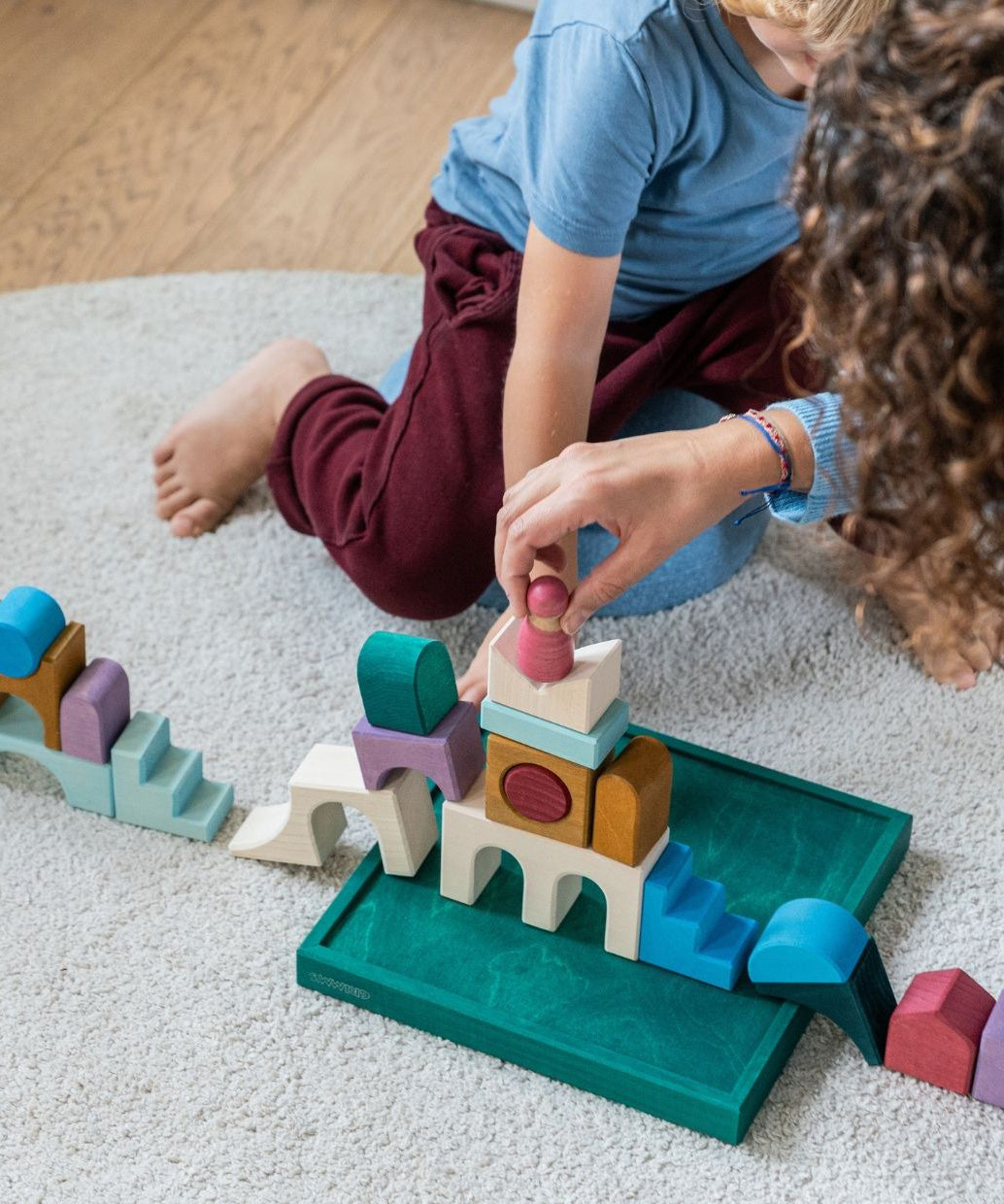 Children playing with pieces from the Grimm's wooden floor building set on the green frame on a fluffy carpet
