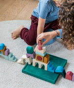 Children playing with pieces from the Grimm's wooden floor building set on the green frame on a fluffy carpet