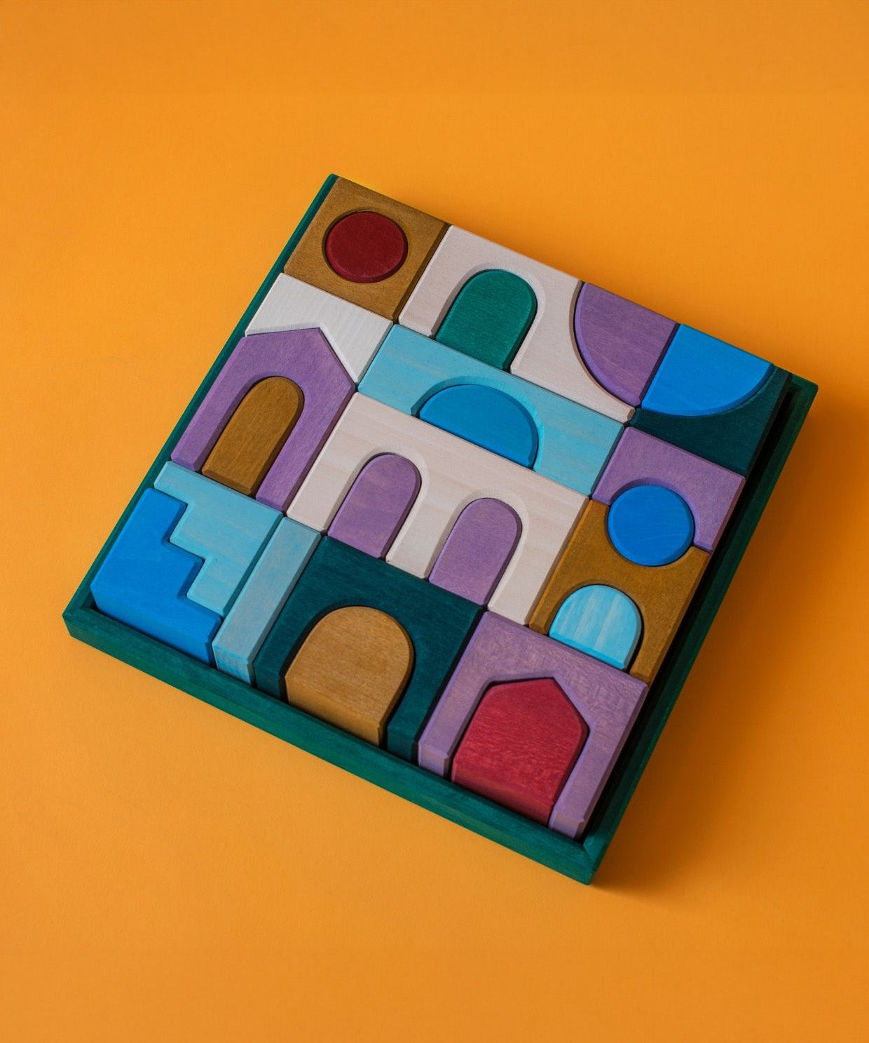 Grimm's wooden floor building set in a green square wooden frame lying flat on a orange surface.