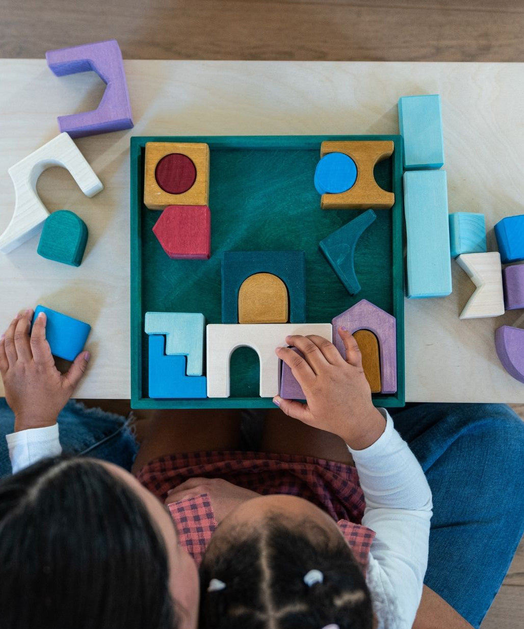 Mother and child arranging different Grimms handcrafted wooden pieces from the floor set on a table