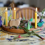 A lovely Grimm's Wooden Celebration Ring display to symbolise an Imbolc tradition. There is a sheep figure, cream coloured candles and green loose parts in the display