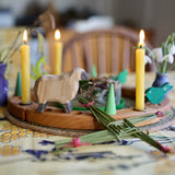 A lovely Grimm's Wooden Celebration Ring display to symbolise an Imbolc tradition. There is a sheep figure, cream coloured candles and green loose parts in the display