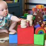 Baby stacking wooden coins on with the Grimm's Large Coloured Boxes Set.