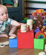 Baby stacking wooden coins on with the Grimm's Large Coloured Boxes Set.
