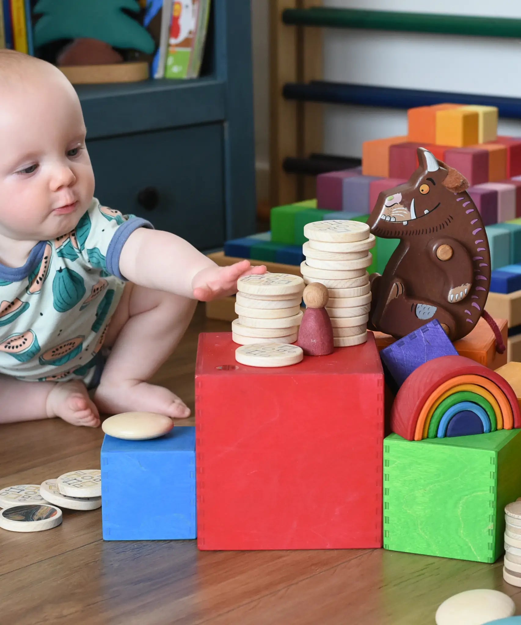 Baby stacking wooden coins on with the Grimm's Large Coloured Boxes Set.