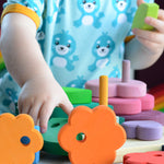 A child is playing with the Grimm's Stacking Flowers Tower. The child has taken some of the flowers off the stacker and is using them to play with