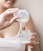 A person pouring milk from the Haakaa Ladybug Silicone Breast Milk Collector, into a Haakaa baby bottle
