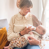 A baby feeding from the Hevea Glass Baby Bottle 120 ml on parents lap.