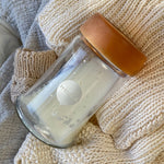 Hevea Wide Neck Glass Baby Bottle with Natural Rubber Cap on a white knitted blanket. 