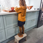 Child in yellow tights preparing food stood on a Hevea Rubberwood Step Stool at a kitchen counter.