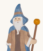 A close up of the Holztiger wooden bearded magician figure showing the hand painted facial features and blue hat while holding  a wooden staff