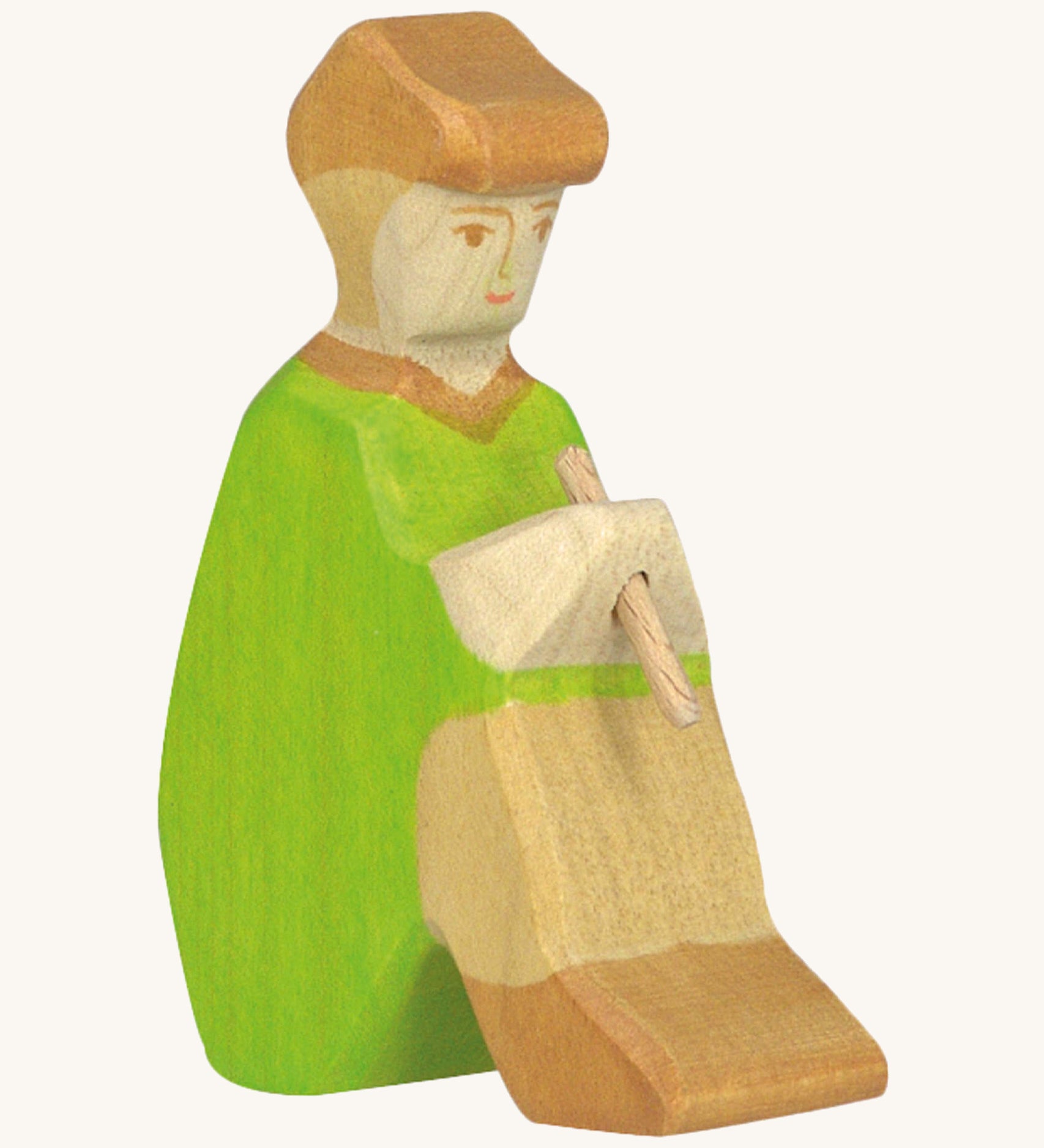 A sitting Holztiger wooden shepherd figure with a hand painted green outfit and brown cap playing a wooden flute