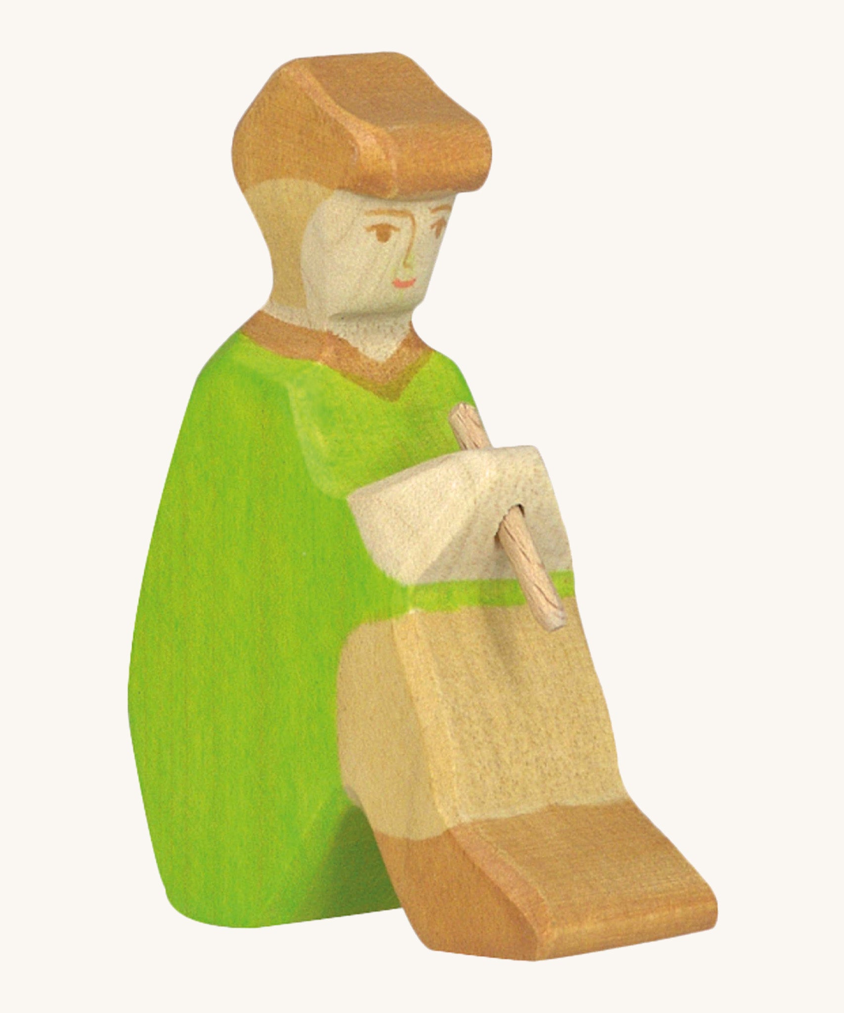 A sitting Holztiger wooden shepherd figure with a hand painted green outfit and brown cap playing a wooden flute