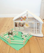 Holztiger Wooden Stable Toy With working Rope Winch, horse stable doors, a ladder and fences. Paired with Holztiger farm animals and a green play cloth from Laura's Play Cotton.