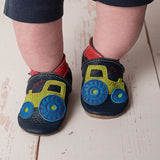 A close up of a child wearing the Inch blue navy tractor baby shoe available at Babipur showing the red ankle cuff detail and the playful green suede tractor design
