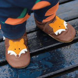 A close up of a baby standing wooden bench and wearing the Inch blue chocolate Mr Fox baby shoe showing the detail on the cute suede fox 