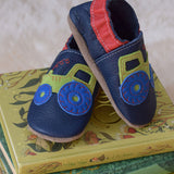 Inch Blue navy tractor baby shoes available at Babipur standing on top of children's story books. 