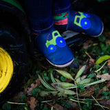 A close up of a child sitting on a tractor and wearing the Inch blue navy tractor baby shoe available at Babipur.
