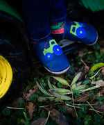 A close up of a child sitting on a tractor and wearing the Inch blue navy tractor baby shoe available at Babipur.