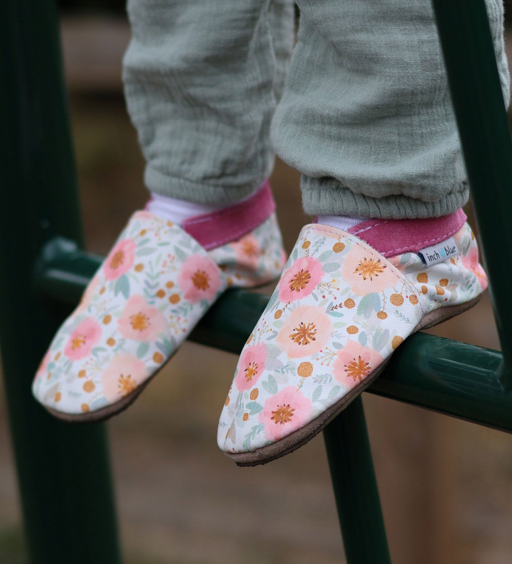 A close up of a child standing on a ladder and wearing the Inch Blue wildroses shoes available at Babipur showing the cute pastel floral design and pink ankle cuff detail