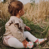 A baby sitting on grass wearing the Inch Blue wildroses shoes available at Babipur. 