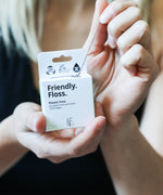 An adult pulling the Jack N Jill friendly dental floss available at Babipur. 100% vegan waxed bamboo activated charcoal & mint dental floss. Features a small cutter on the top of the box for easy cutting.
