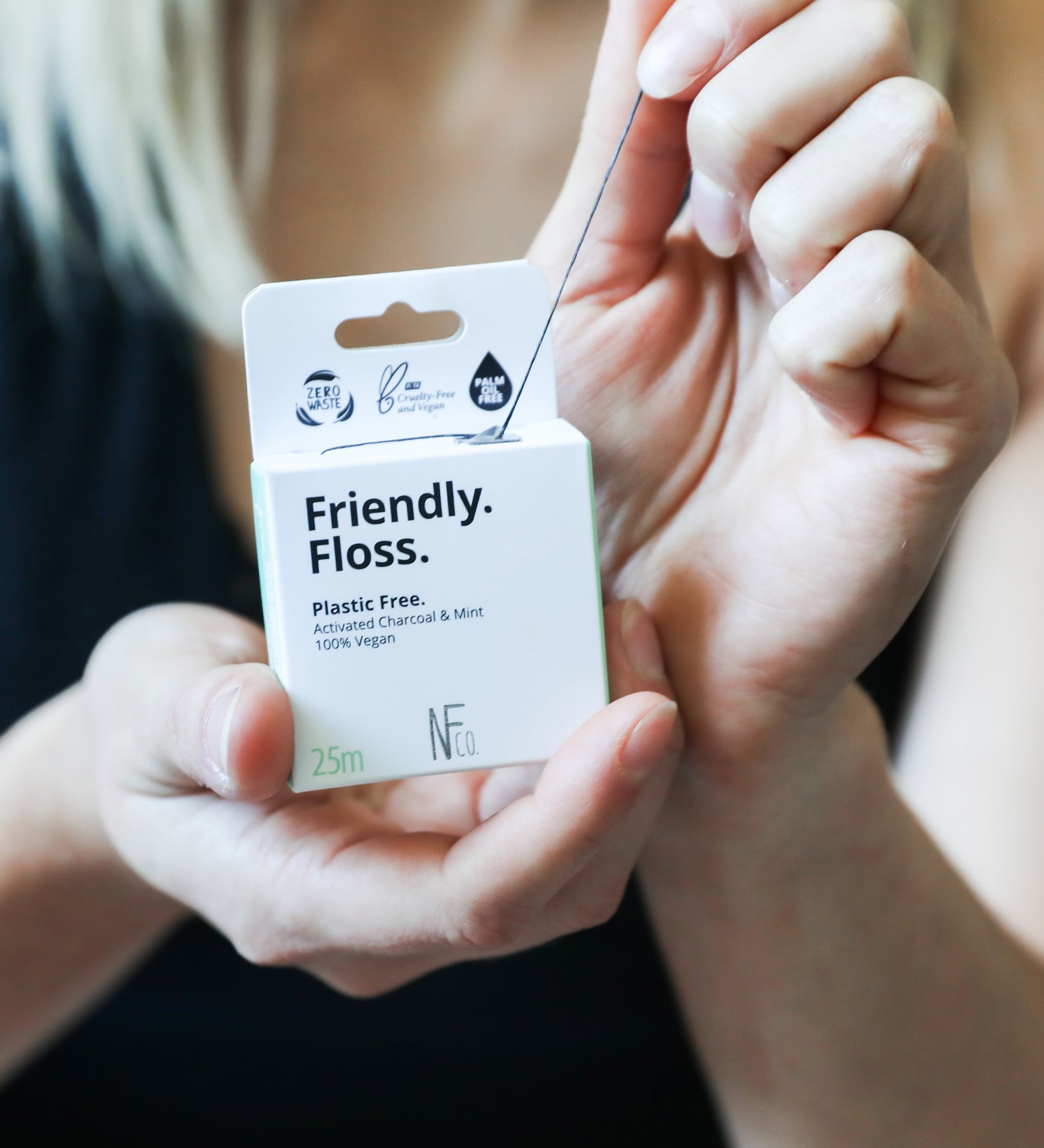 An adult pulling the Jack N Jill friendly dental floss available at Babipur. 100% vegan waxed bamboo activated charcoal & mint dental floss. Features a small cutter on the top of the box for easy cutting.