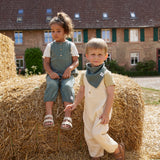 Two children sat on haybales, wearing Lassig organic cotton muslin jumpsuits. 