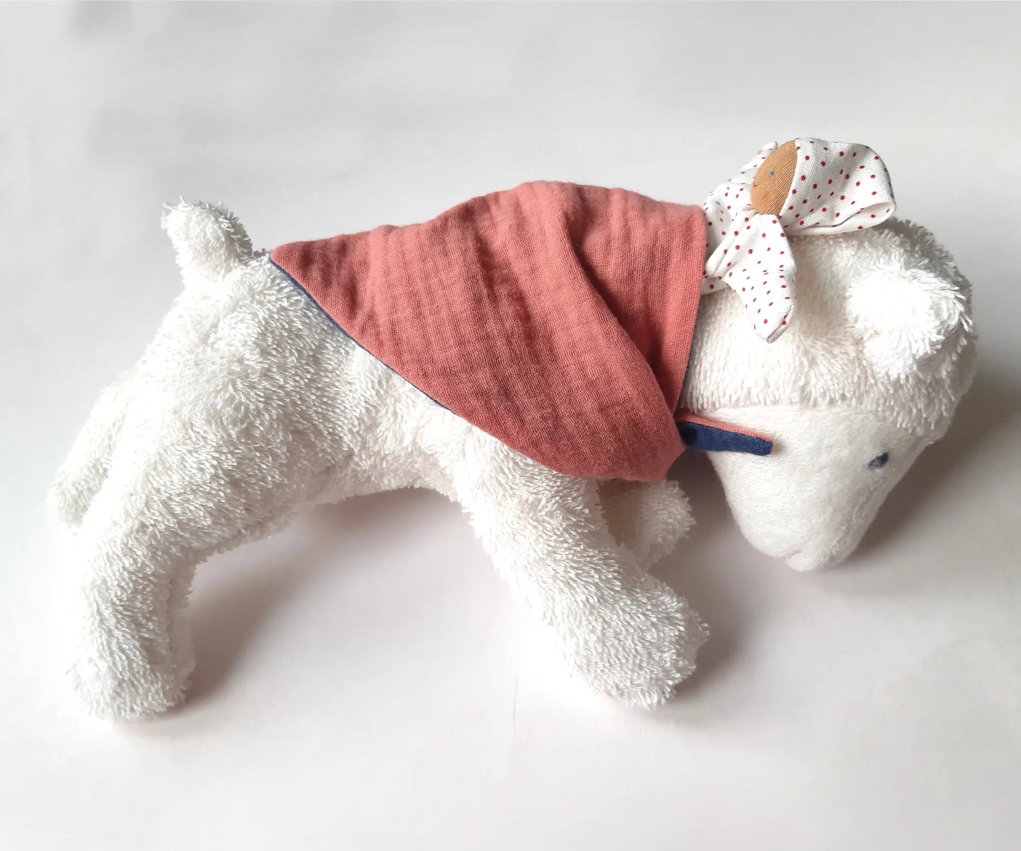 Kathe Kruse white lying lamb comforter with small white waldorf doll on the back wrapped in the muslin bib
