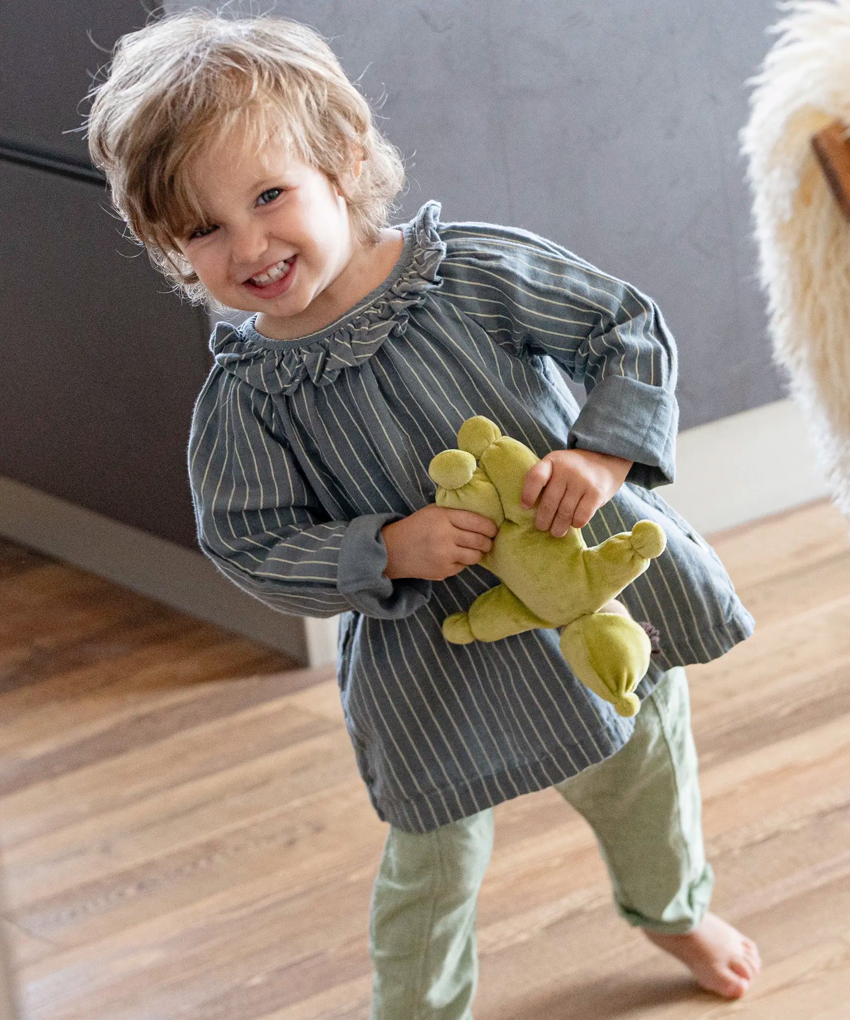 Child playing with Kathe Kruse light green Lolo moss Waldorf doll in a dining room