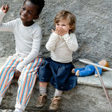 Children sitting on a wall next to a lying Kathe Kruse nana cloud waldorf doll on a concrete wall