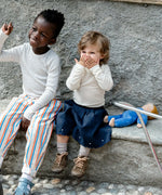 Children sitting on a wall next to a lying Kathe Kruse nana cloud waldorf doll on a concrete wall