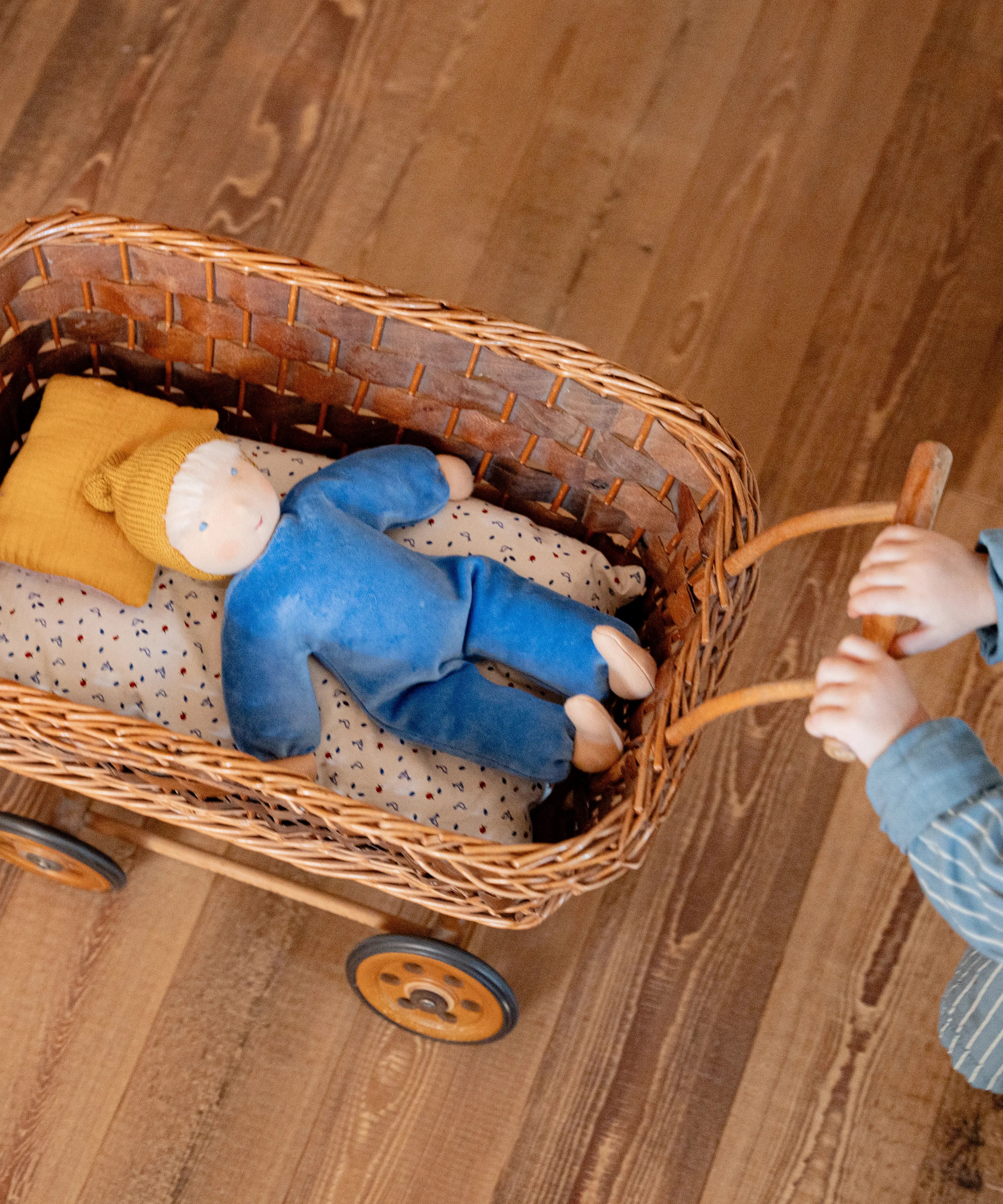 Child pushing a wicket pram with a Kathe kruse cloud nana waldorf doll lying inside 