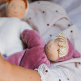 Child holding a Kathe Kruse Lolo Rose waldorf doll showing a light pink towelling outfit, light skin and yellow hair.
