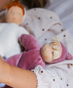 Child holding a Kathe Kruse Lolo Rose waldorf doll showing a light pink towelling outfit, light skin and yellow hair.