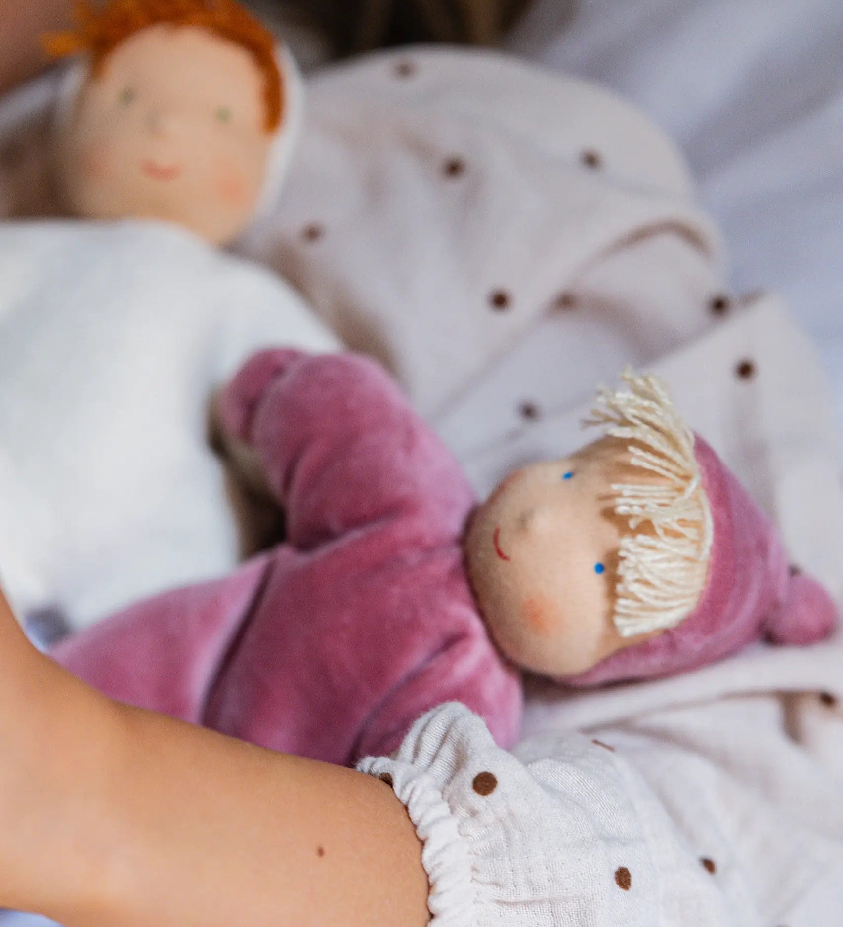 Child holding a Kathe Kruse Lolo Rose waldorf doll showing a light pink towelling outfit, light skin and yellow hair.