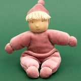 Kathe Kruse Lolo Rose waldorf doll showing a light pink towelling outfit, sitting in front o a green background