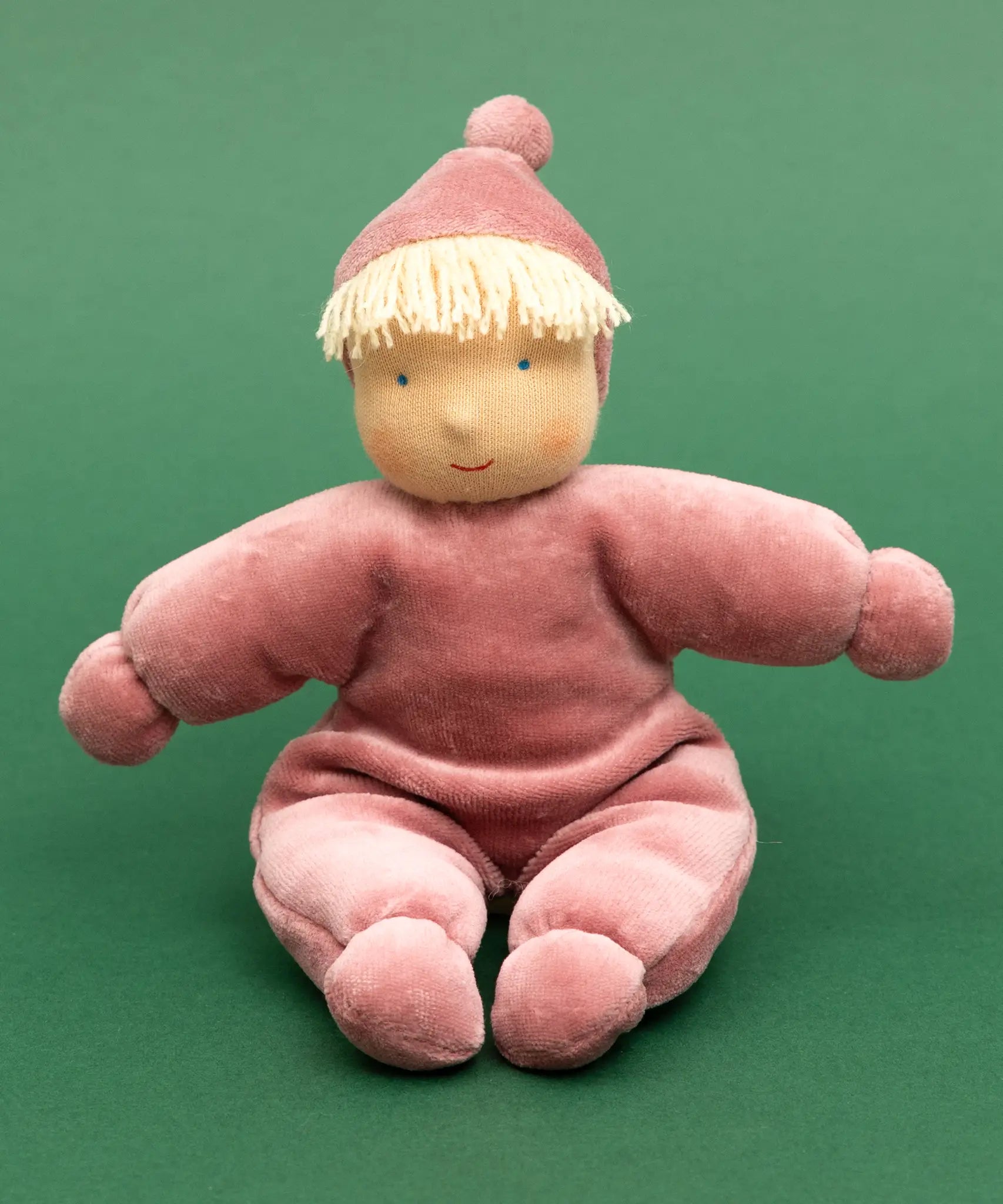Kathe Kruse Lolo Rose waldorf doll showing a light pink towelling outfit, sitting in front o a green background
