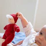 Baby holding the Kathe Kruse Lolo Ruby Waldorf doll showing the red towelling outfit, light skin and white hair.