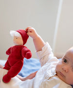 Baby holding the Kathe Kruse Lolo Ruby Waldorf doll showing the red towelling outfit, light skin and white hair.
