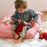 Child playing with a red and pink Kathe Kruse Lolo Waldorf dolls on a white blanket.