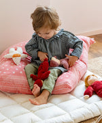 Child playing with a red and pink Kathe Kruse Lolo Waldorf dolls on a white blanket.