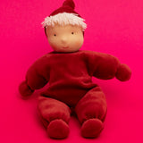 Kathe Kruse Lolo Ruby Waldorf doll showing a red towelling outfit sitting in front of a bright red background.