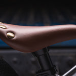 The Early Rider Charger Balance Bike adjustable seat, in a tan brown colour and gold flat rivets on the back of the seat